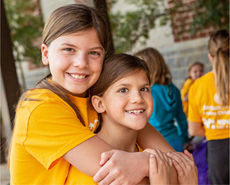 Smiling Girls on the Run participant hugging another smiling participant from behind
