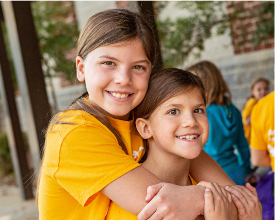 Smiling Girls on the Run participant hugging another smiling participant from behind