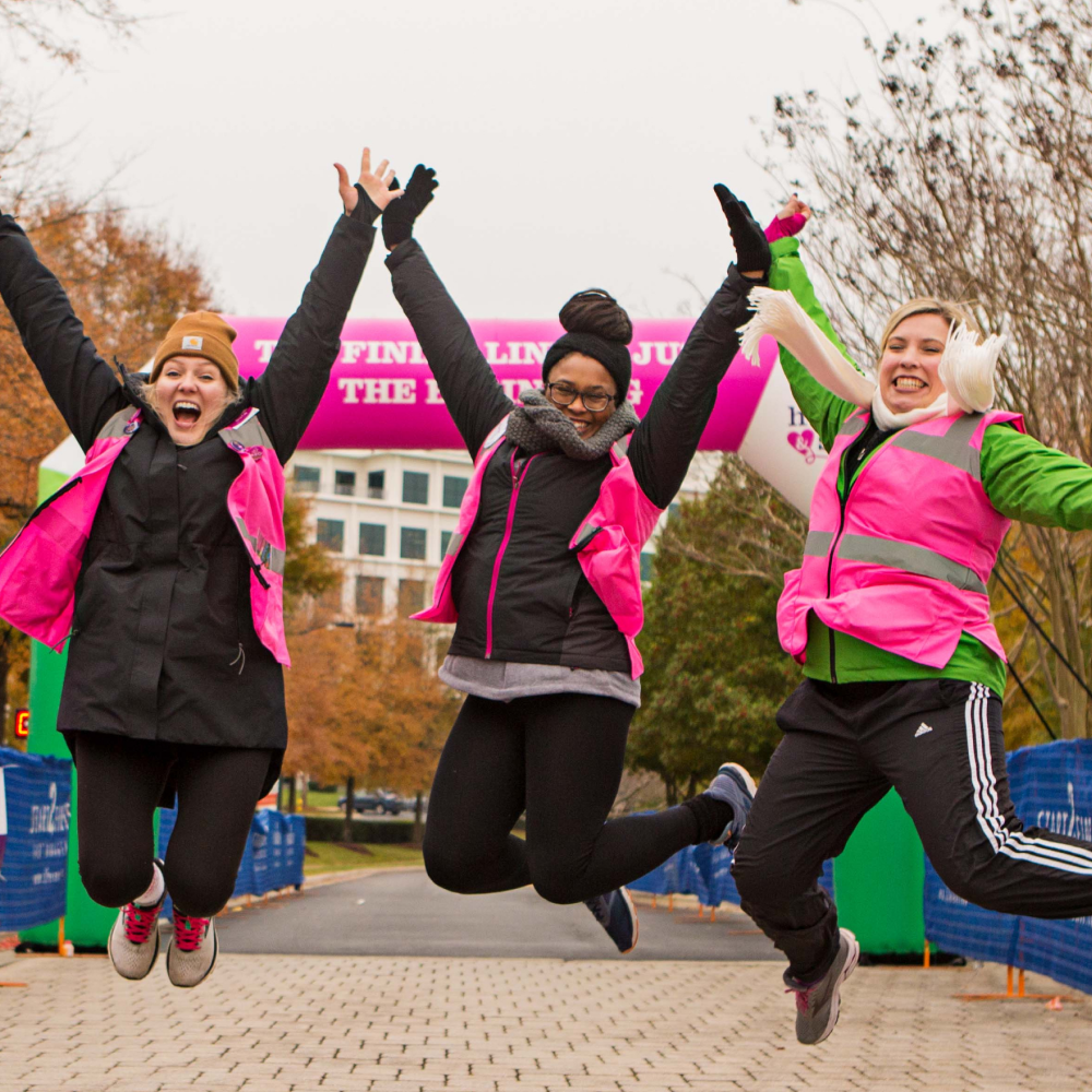 Three Girls on the Run 5K volunteers jumping at the race finish line